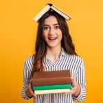 Portrait of a cheerful young girl holding books isolated over yellow background